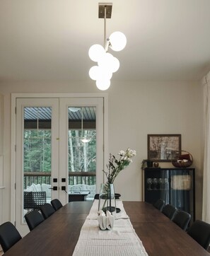 A dining room with a large table, chairs, a vase with flowers, and a hanging light fixture. - Beautiful Muskoka Cottage with Games, BBQ & Views (Huntsville)