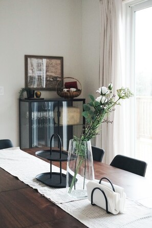 A dining table with a clear glass vase containing white flowers, a black tray stand, and a white tray with a black handle. - Beautiful Muskoka Cottage with Games, BBQ & Views (Huntsville)