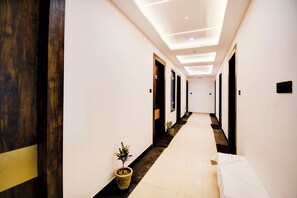 A hotel hallway with a modern design, featuring a long corridor, wooden doors, and a potted plant.