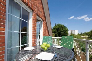 Ein Balkon mit einem Tisch für zwei Personen, einer Schüssel grüner Äpfel und einem Fenster mit Blick auf Häuser und Bäume.