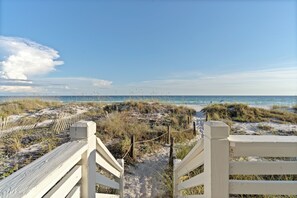 Ein hölzerner Steg führt zu einem Strand mit Dünen und Gräsern.
