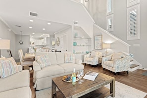 A spacious living room with a large sectional sofa, a wooden coffee table, and a staircase leading to an upper level. - Beachfront + Private Beach + Chair Service + 3 Decks | Gulf Views | Seawinds 1 (Miramar Beach)