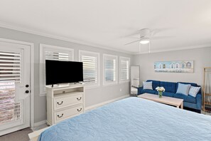 Een slaapkamer met een bed, een televisie op een dressoir, een blauwe bank en een schilderij aan de muur.