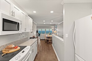 A modern kitchen with white cabinetry, a microwave, an oven, and a dining area with a view of the sea. - Beachfront + Private Beach + Chair Service + 3 Decks | Gulf Views | Seawinds 1 (Miramar Beach)