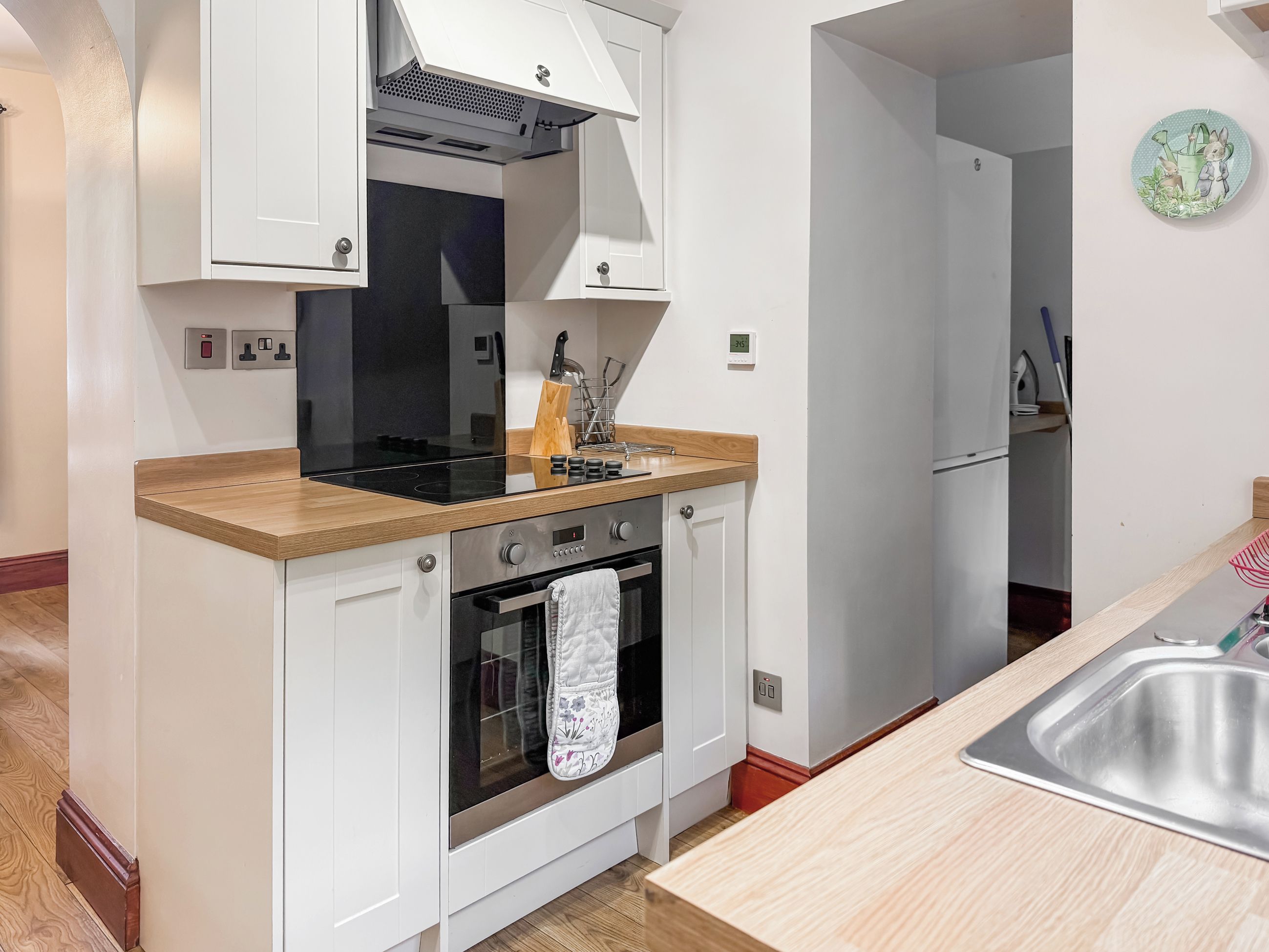 A compact kitchen with white cabinetry, a black stove, and a wooden countertop.