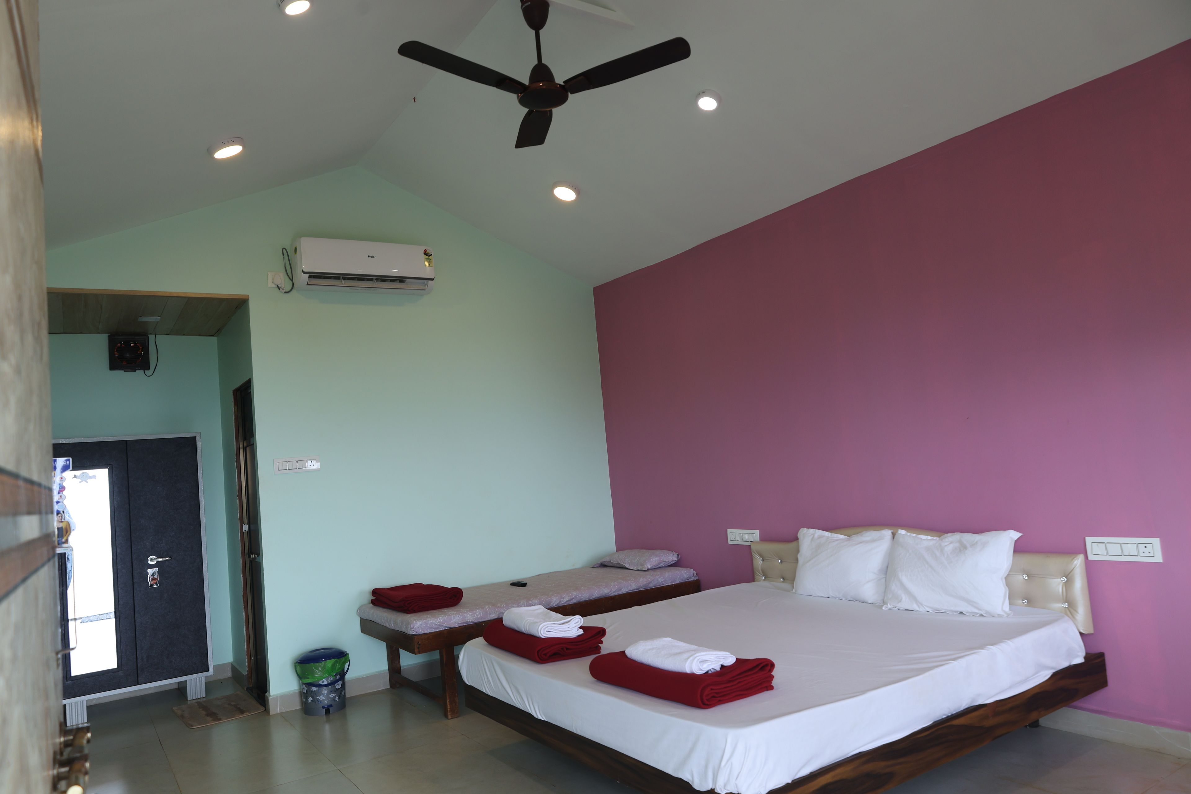 A hotel room with a bed, two bedside tables, a ceiling fan, an air conditioning unit, and a door leading to another room.