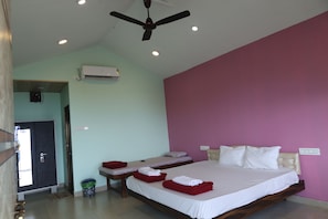 A hotel room with a bed, two bedside tables, a ceiling fan, an air conditioning unit, and a door leading to another room.