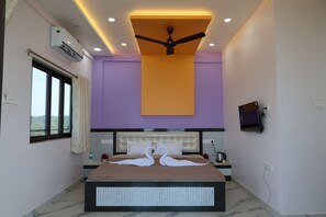 A hotel room with a bed, a ceiling fan, an air conditioning unit, a TV mounted on the wall, and a window with a view.