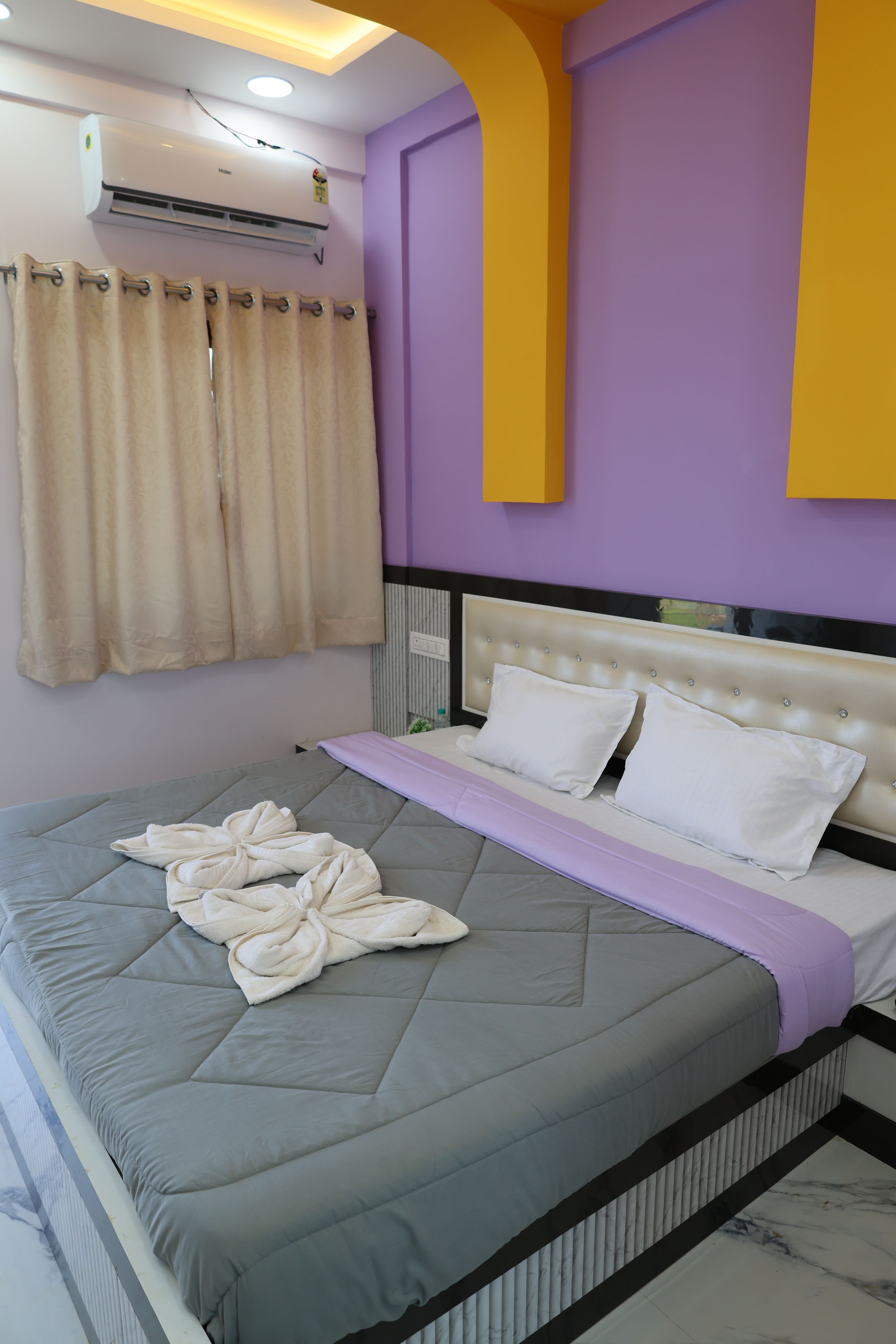 Habitació d'hotel amb un llit, una finestra amb cortines, un aparell d'aire condicionat i una paret amb un toc de color groc.