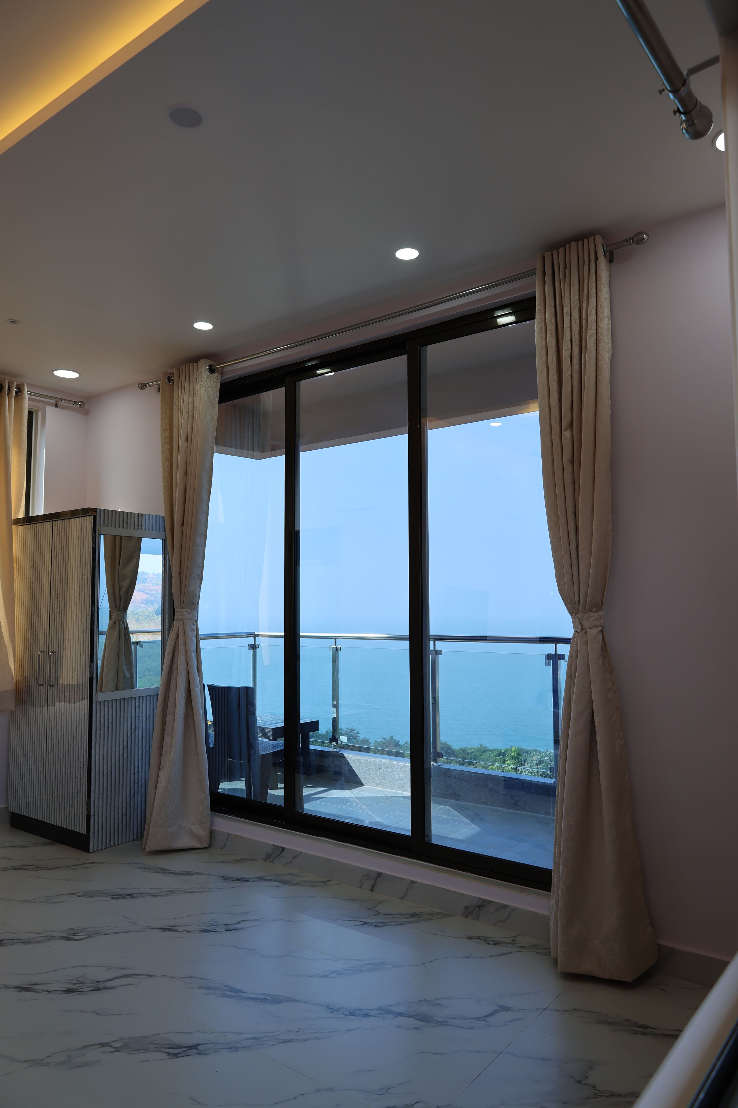 Un balcón con vistas al mar, suelo de mármol y puerta corredera moderna.