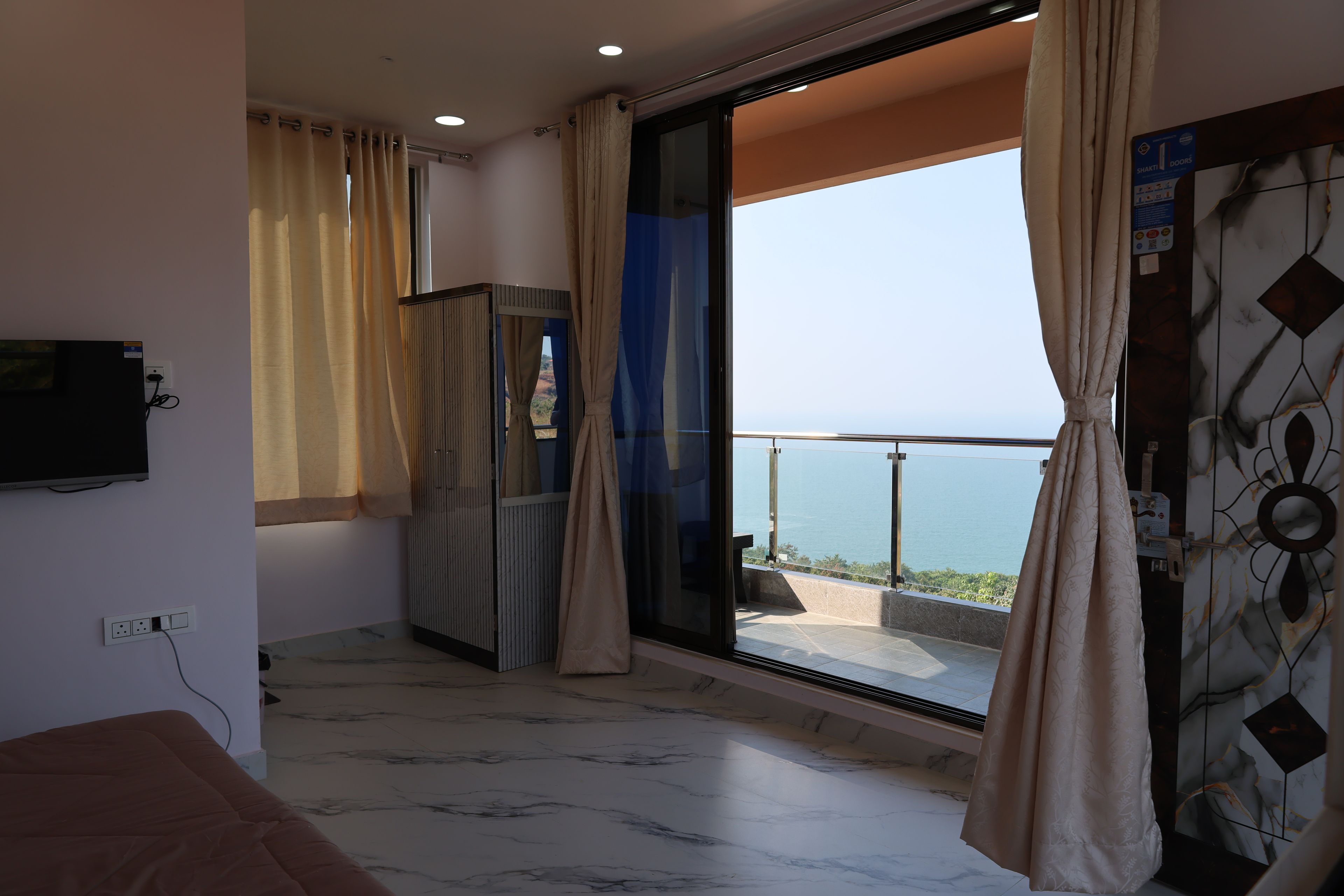 A hotel room with a large sliding glass door leading to a balcony with a view of the sea.