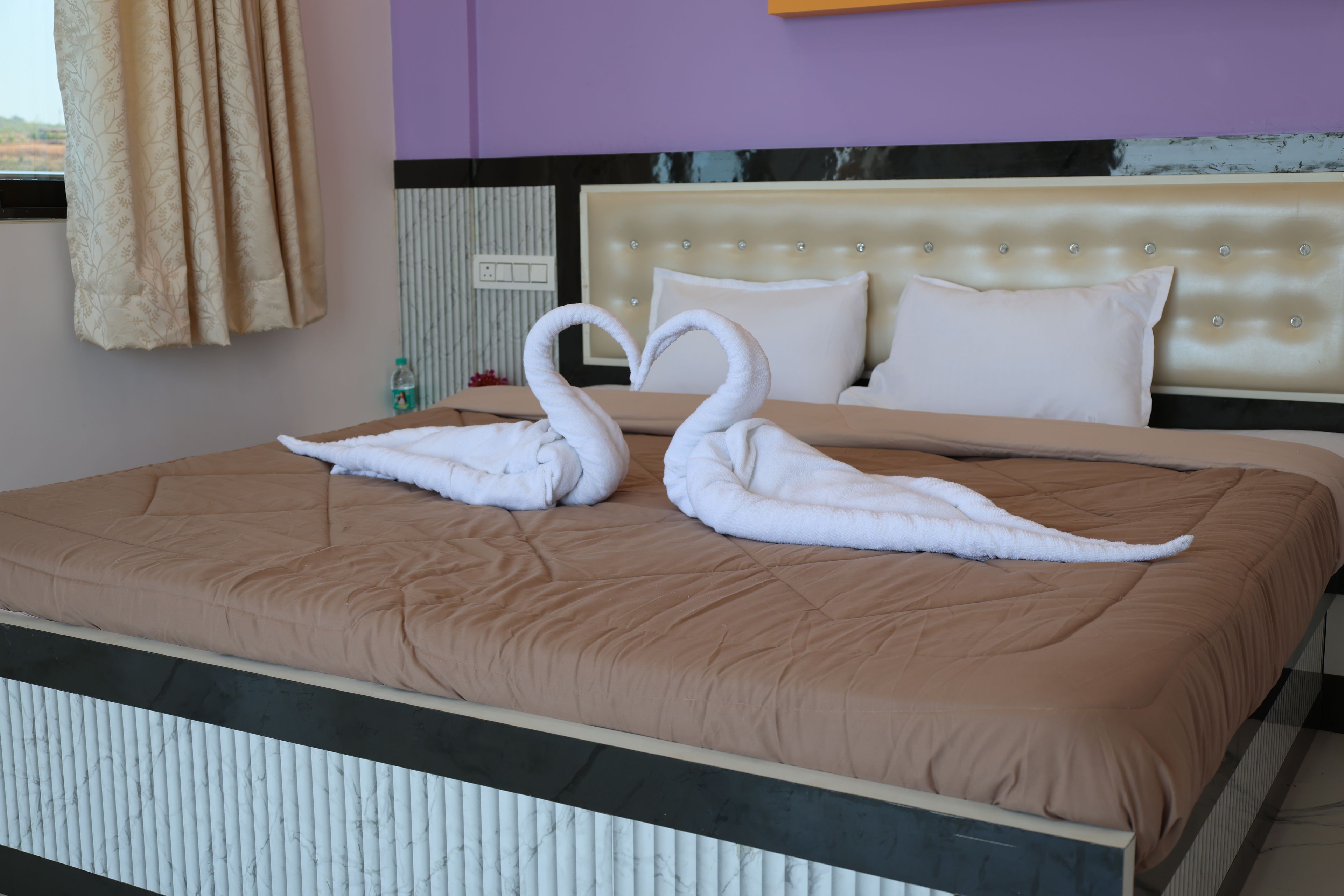 A bed with a brown bedspread and two swan-shaped towels.