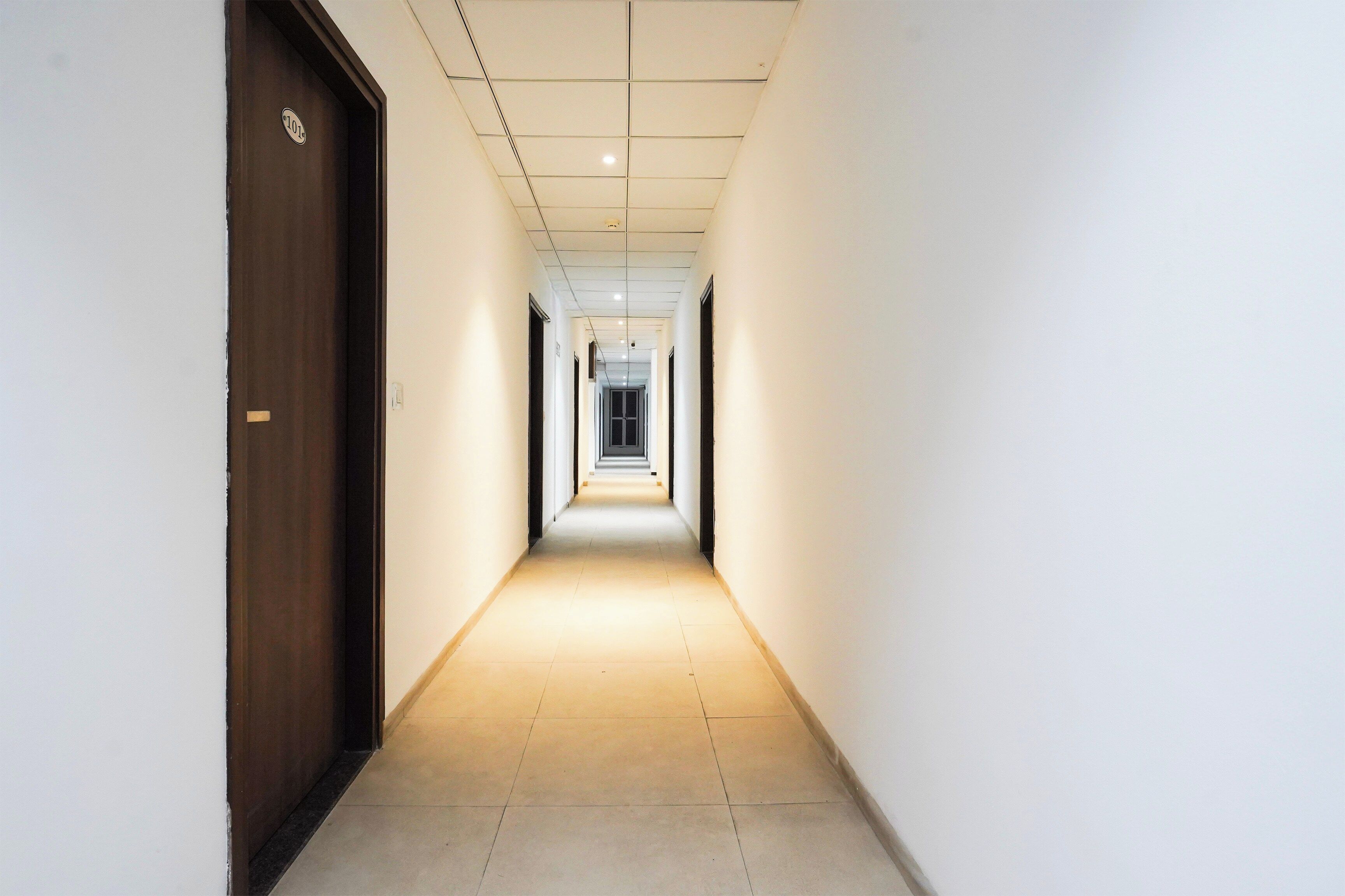 A corridor with a wooden door on the left and a light-colored tiled floor.