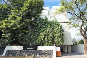 Una casa de apartamentos con entrada de muro de piedra, un letrero que indica servicio de empresa y un árbol grande al frente.