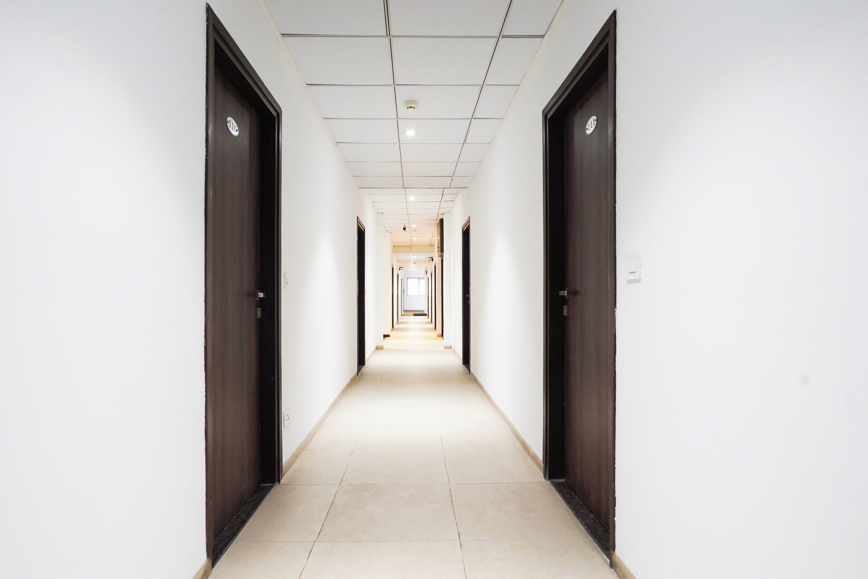 Un pasillo largo y estrecho con puertas a ambos lados, que conduce a una habitación luminosa al final.