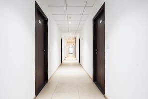 A long, narrow hallway with doors on both sides, leading to a bright room at the end. - Super Townhouse Central Bazar Road (Nagpur)
