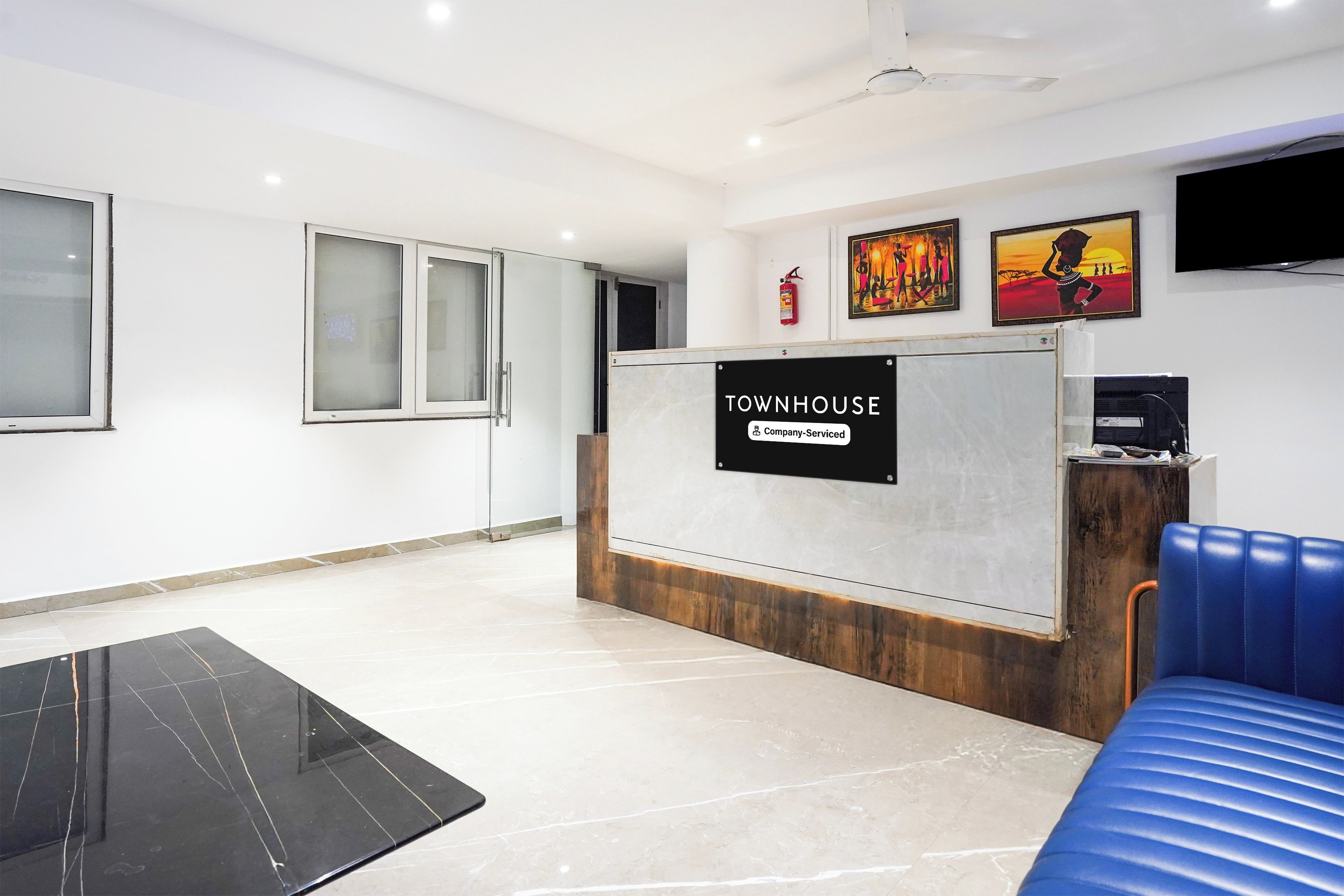 A reception area with a sign reading 'TOWNHOUSE Company-Serviced,' a flat-screen TV, and artwork on the wall.