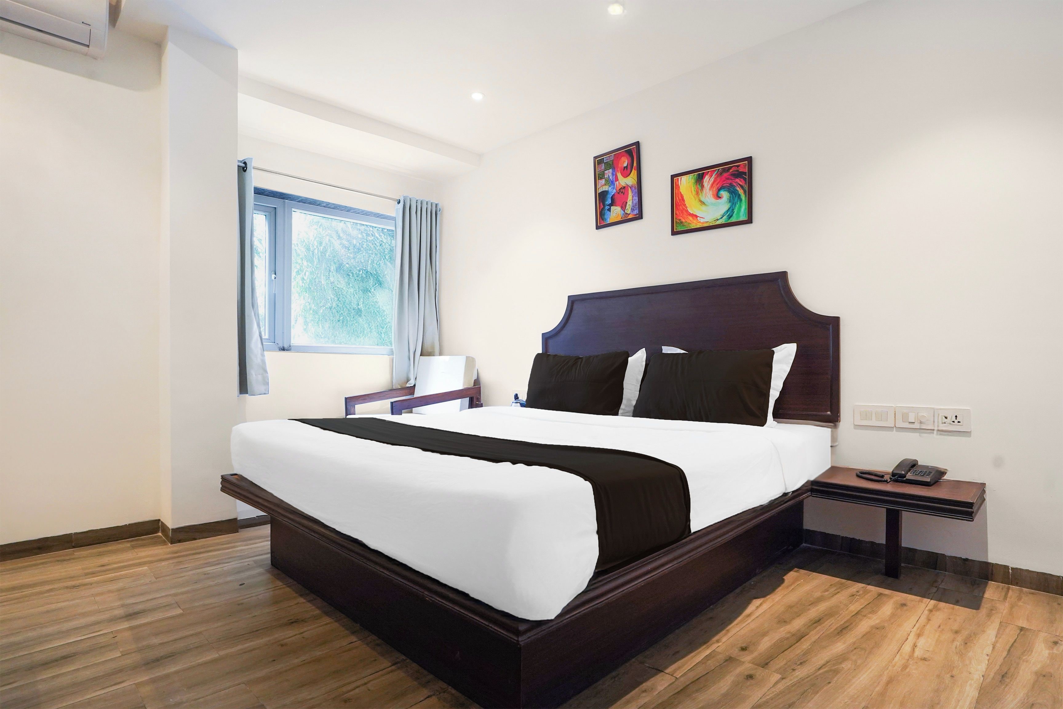 Ein Hotelzimmer mit einem großen Bett, einem Nachttisch, Vorhängen vor einem Fenster und zwei Wandbildern.