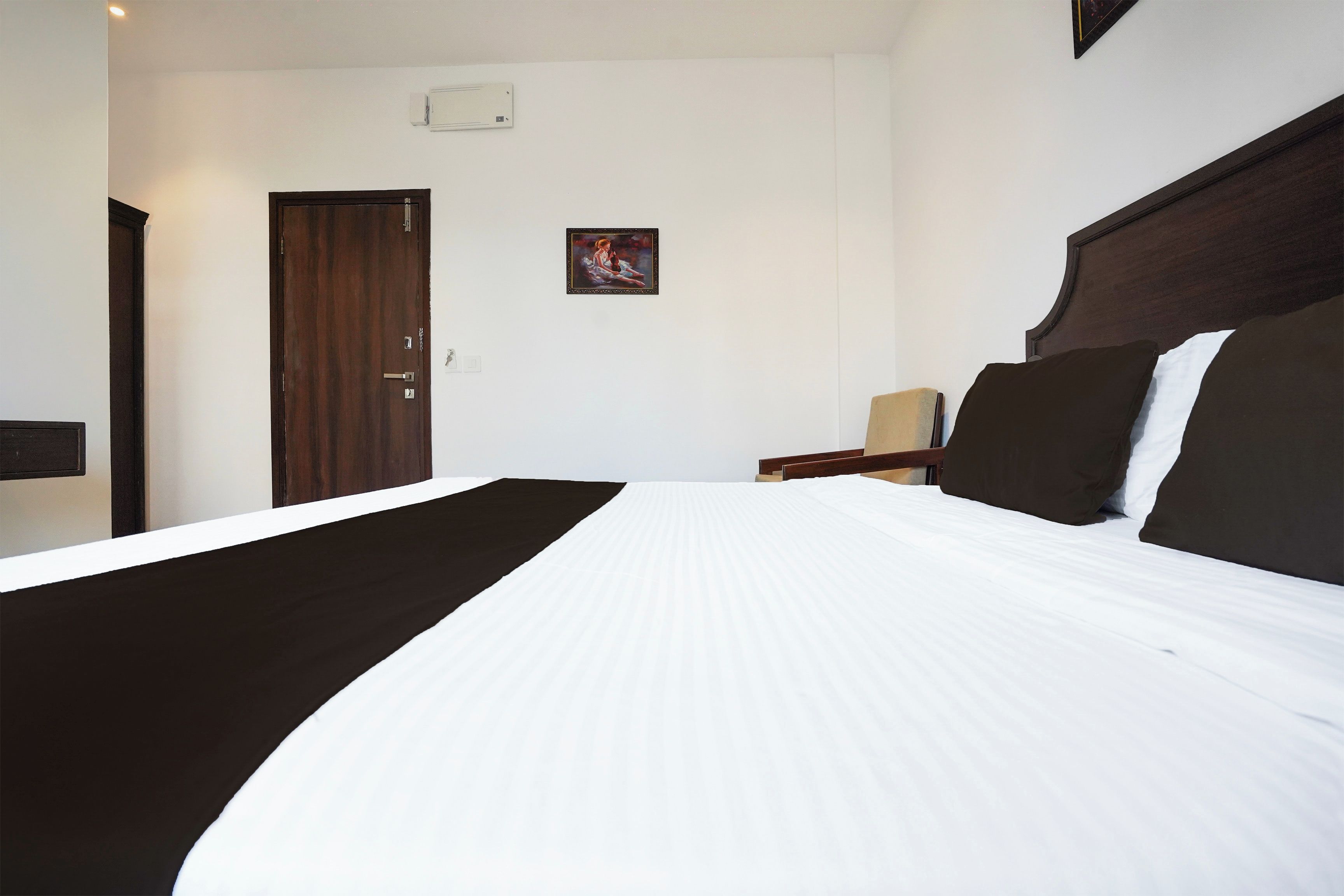 Habitación de hotel con una cama grande, una puerta de madera, una mesita con una silla y un equipo de aire acondicionado instalado en la pared.