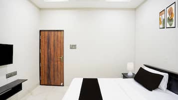 Una habitación de hotel con una cama, mesita de noche, lámpara y televisor en la pared.