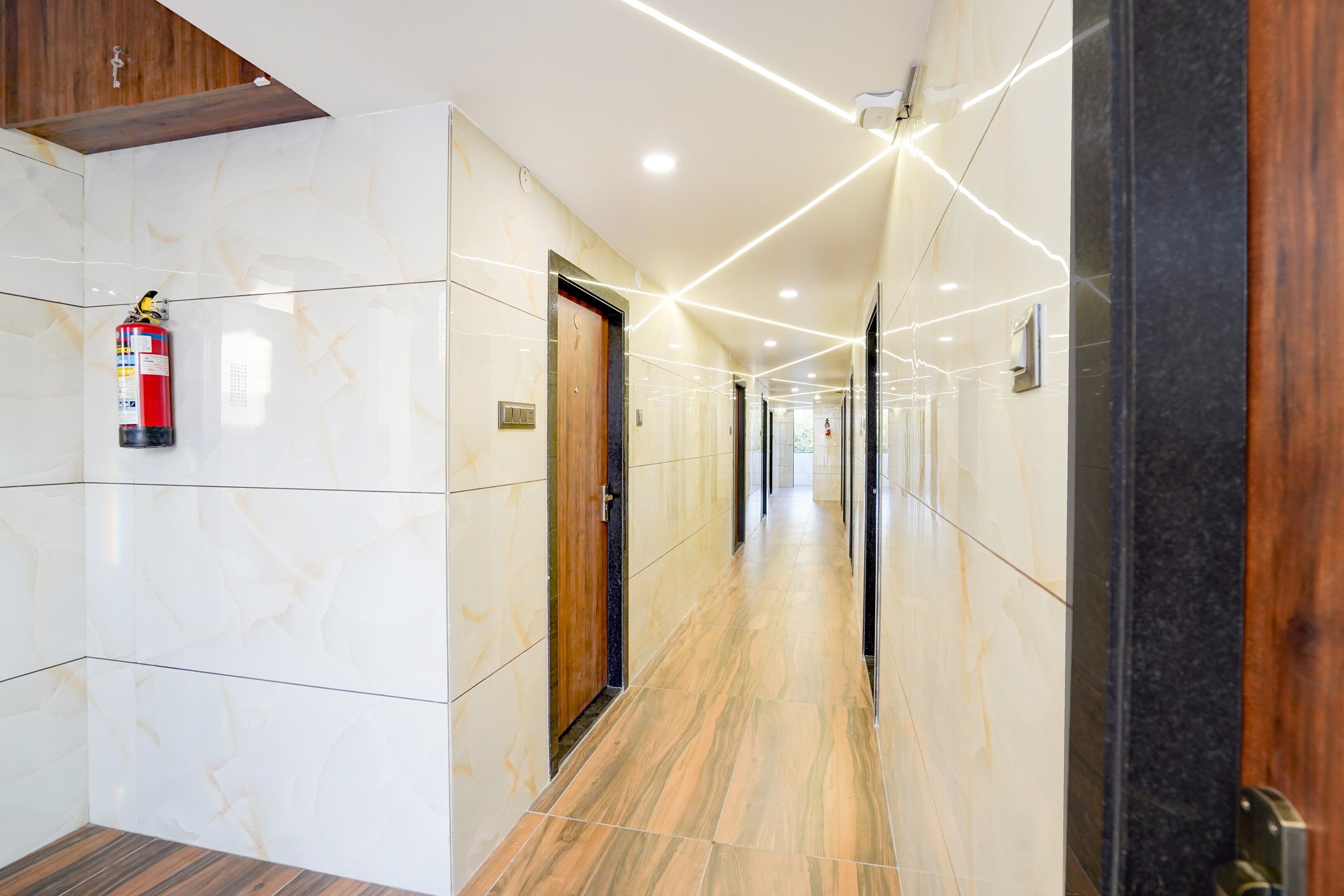 A hotel corridor with marble walls, wooden doors, and a fire extinguisher.