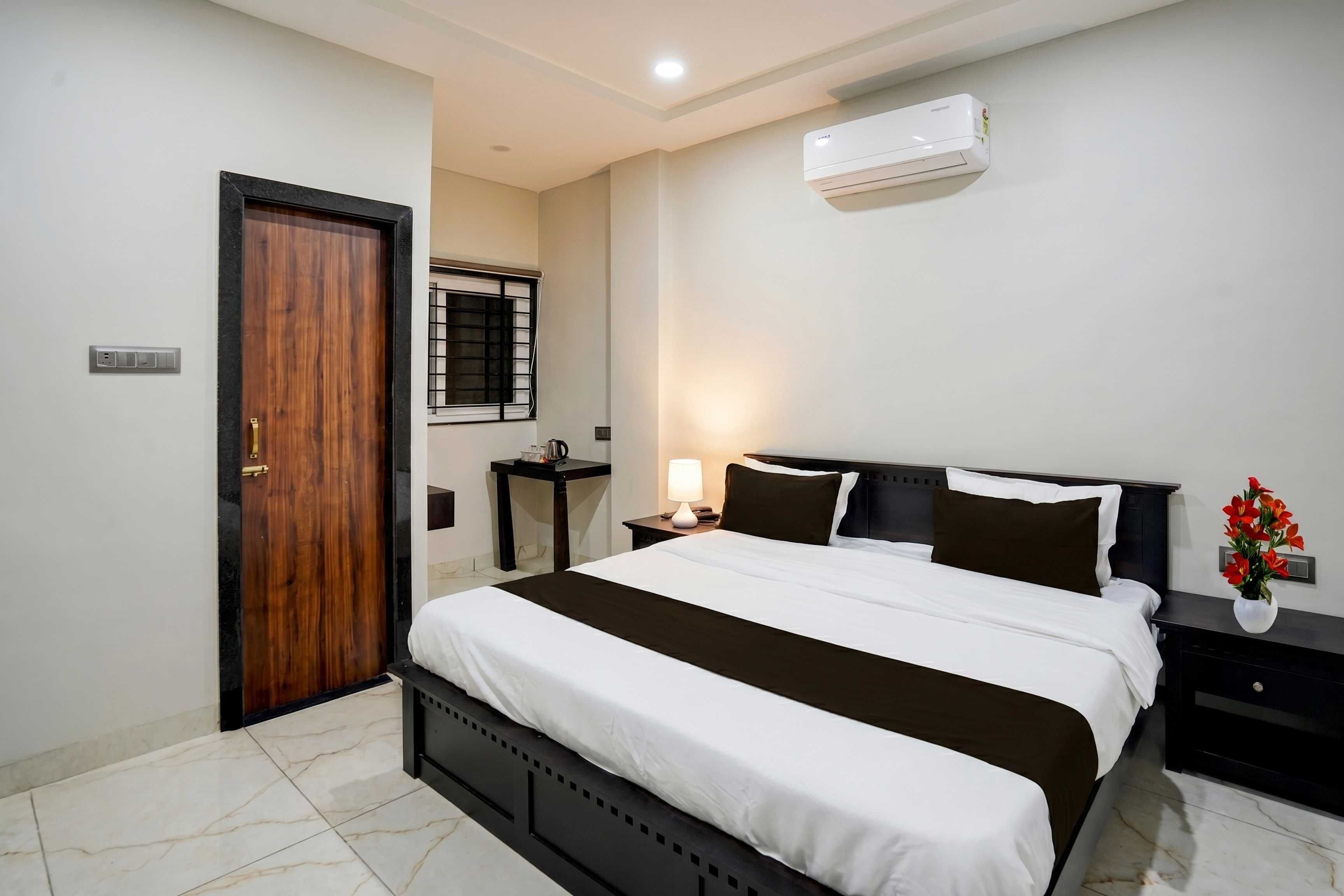 A hotel room with a bed, bedside tables, a nightstand, an air conditioner, a window with bars, and a door.