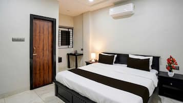 A hotel room with a bed, bedside tables, a nightstand, an air conditioner, a window with bars, and a door.