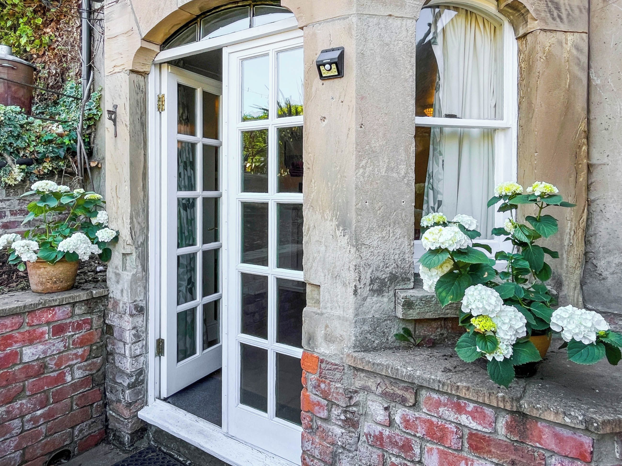 Un bâtiment traditionnel avec une porte blanche, une fenêtre ornée de rideaux et des plantes en pot aux fleurs blanches.
