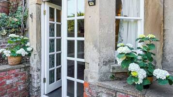 A traditional building with a white door, a window with curtains, and potted plants with white flowers.