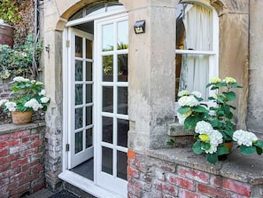 Un bâtiment traditionnel avec une porte blanche, une fenêtre ornée de rideaux et des plantes en pot aux fleurs blanches.