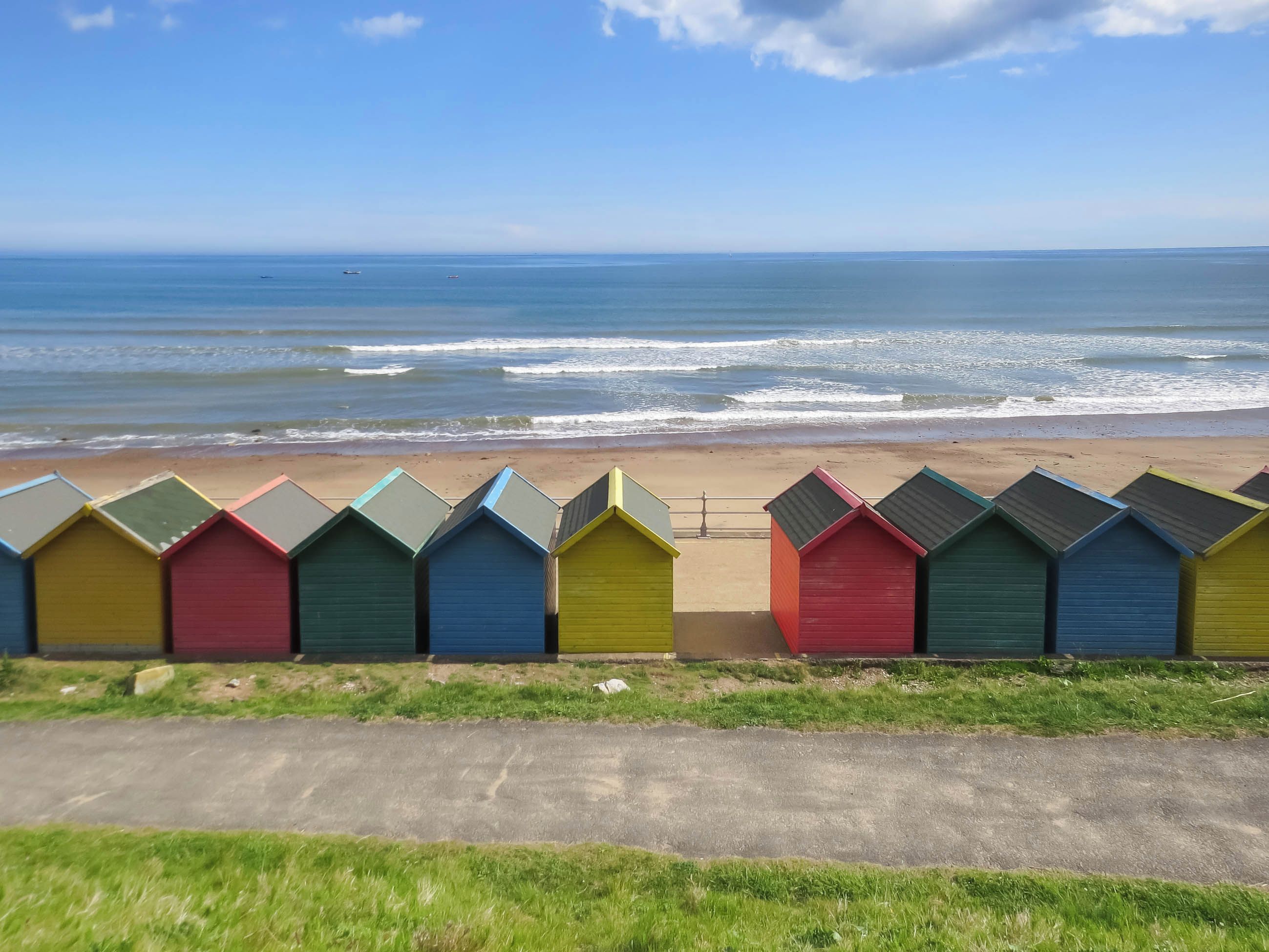 Een rij kleurrijke strandhuisjes langs een kustweg, met de zee op de achtergrond.