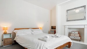 A neatly made bed in a hotel room with a wooden headboard, two bedside lamps, a television, and a mirror above a fireplace. - 1 bedroom accommodation in Whitby (Whitby)