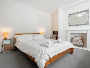 Cama bien hecha en una habitación de hotel con cabecera de madera, dos lámparas de noche, televisor y espejo sobre una chimenea.