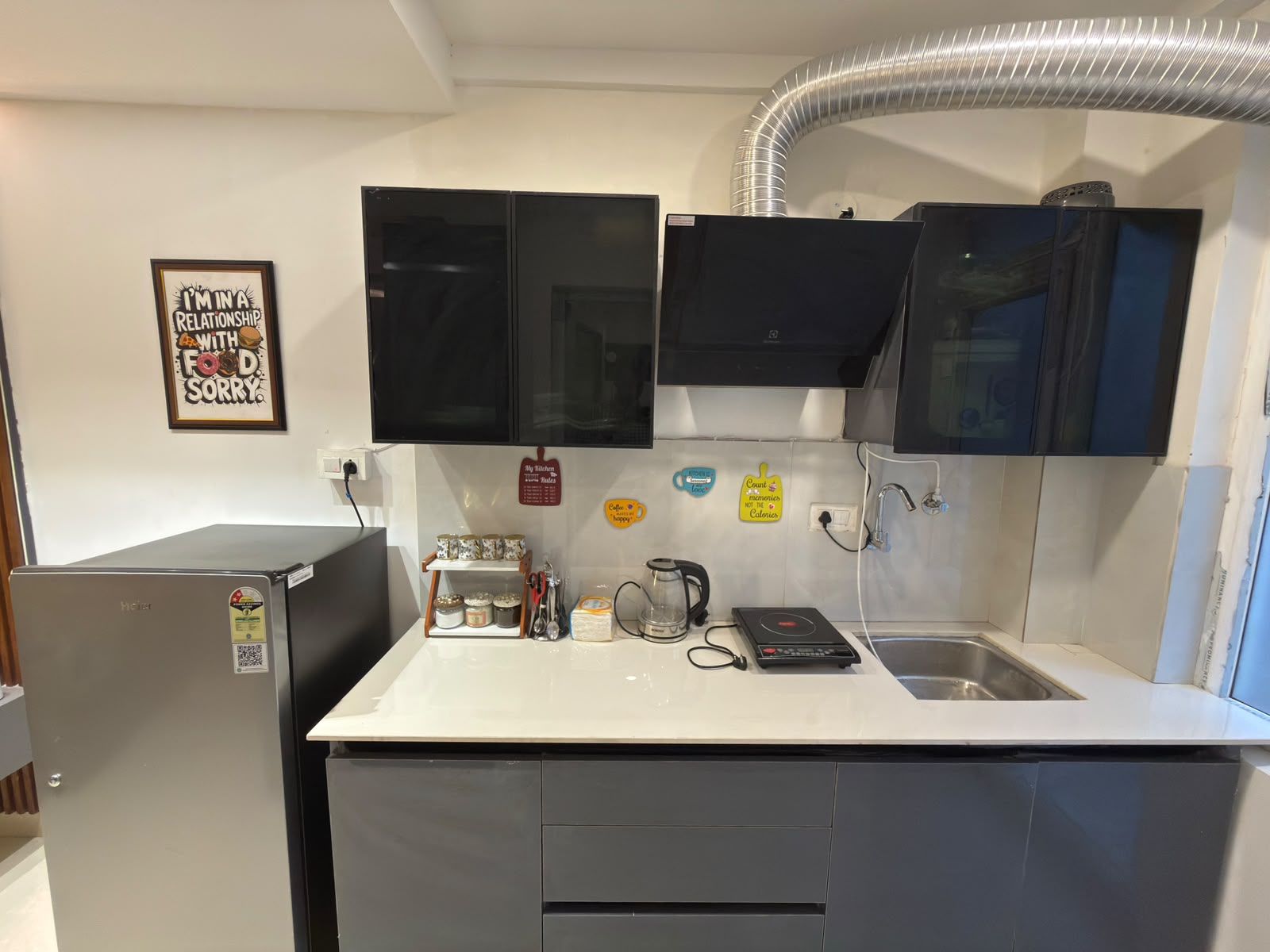 A compact kitchen with a refrigerator, microwave, and a coffee maker. There are cabinets above the counter and a sink with a faucet.