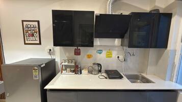 A compact kitchen with a refrigerator, microwave, and a coffee maker. There are cabinets above the counter and a sink with a faucet.