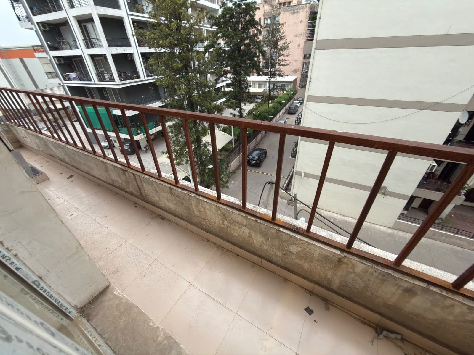 A balcony with a metal railing overlooking a street with parked cars and buildings.