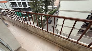 A balcony with a metal railing overlooking a street with parked cars and buildings.