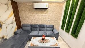 Uma sala de estar com um sofá seccional cinza, uma mesa de centro branca com detalhes dourados e um ar-condicionado fixado na parede.