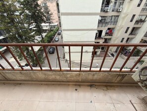 A balcony with a metal railing overlooking a street with parked cars and buildings.