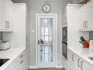 A modern kitchen with white cabinetry, a frosted glass door, a clock, and a toaster on the counter. - 2 bedroom accommodation in Devon, Sidmouth, Salcombe Regis, Budleigh Salterton, Seaton (Devon, Sidmouth, Salcombe Regis, Budleigh Salterton, Seaton)