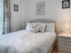 Ein ordentlich bezogenes Bett mit gesteppter Decke, ein Nachttisch mit Lampe und eine Wand mit gerahmten Bildern.
