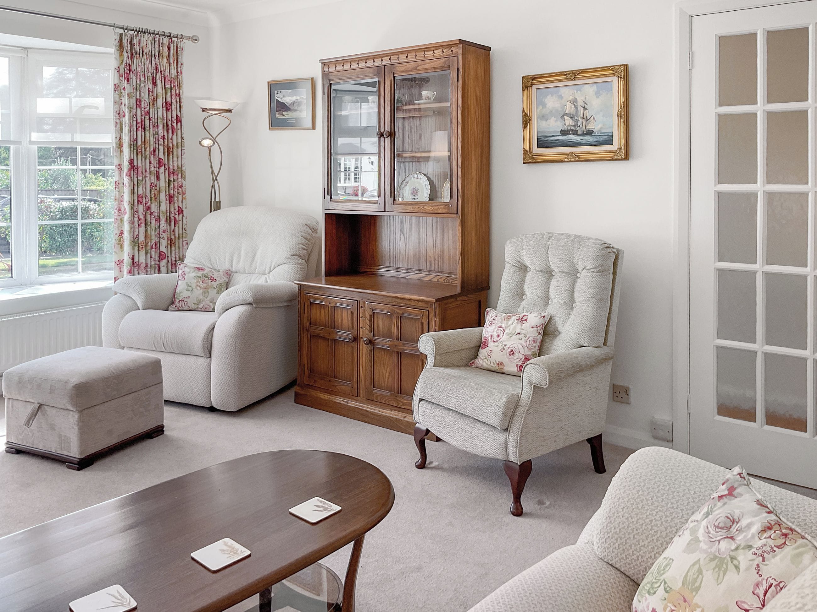 A living room with a sofa, armchair, ottoman, wooden cabinet, and a table.
