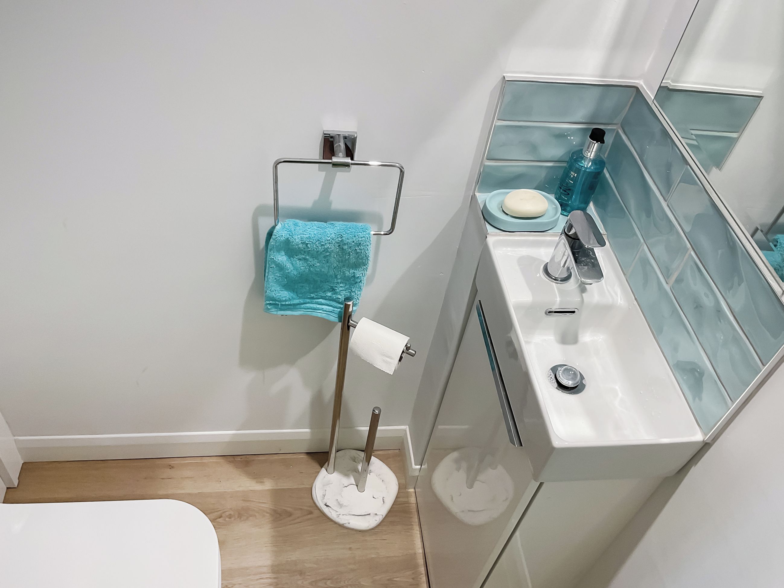 Ein Badezimmer mit einem weißen Waschbecken, einem Spiegel, einem Handtuchhalter mit einem blauen Handtuch und einer Seifenschale.