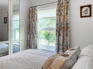 A bedroom with a bed, floral curtains, a window, and a framed picture on the wall. - 2 bedroom accommodation in Devon, Sidmouth, Salcombe Regis, Budleigh Salterton, Seaton (Devon, Sidmouth, Salcombe Regis, Budleigh Salterton, Seaton)