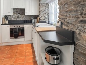A kitchen with white cabinets, a stone accent wall, a black countertop, and a slow cooker. - 2 bedroom accommodation in St Columb Major (St Columb Major)