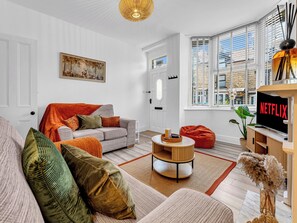A modern living room with a sofa, a coffee table, and a television displaying 'NETFLIX'. - A terraced cottage on Bennett Street, in the heart of Buxton. (Buxton)