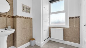 A bathroom with a white sink, a toilet, a window with a view, and a tiled wall. - A terraced cottage on Bennett Street, in the heart of Buxton. (Buxton)