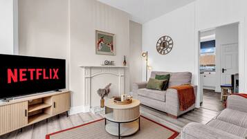 A modern living room with a television displaying 'NETFLIX,' a fireplace, a sofa, and a dining area with a view.