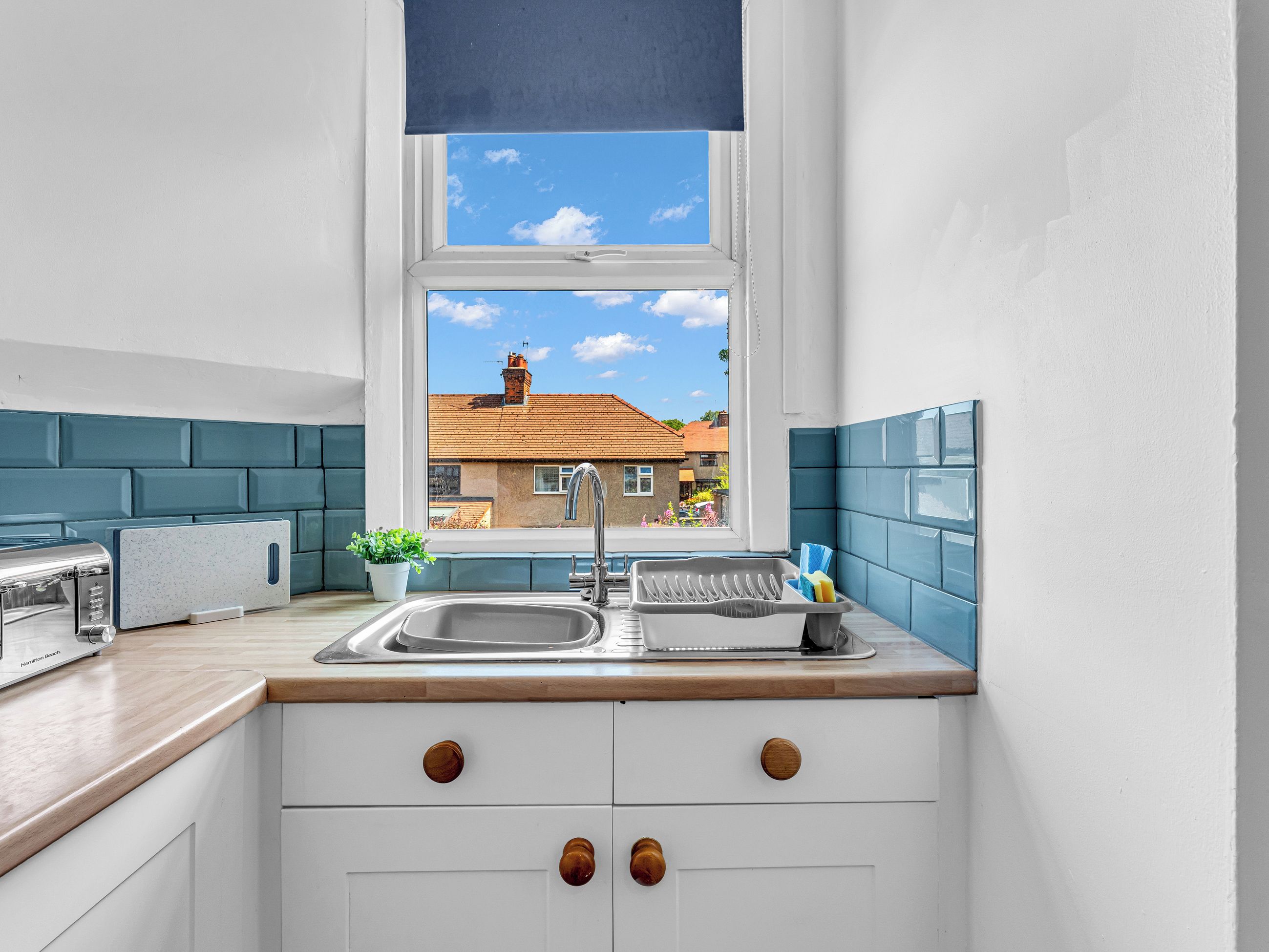 A compact kitchen with a window, a sink, a toaster, and a potted plant.