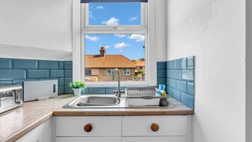 A compact kitchen with a window, a sink, a toaster, and a potted plant.